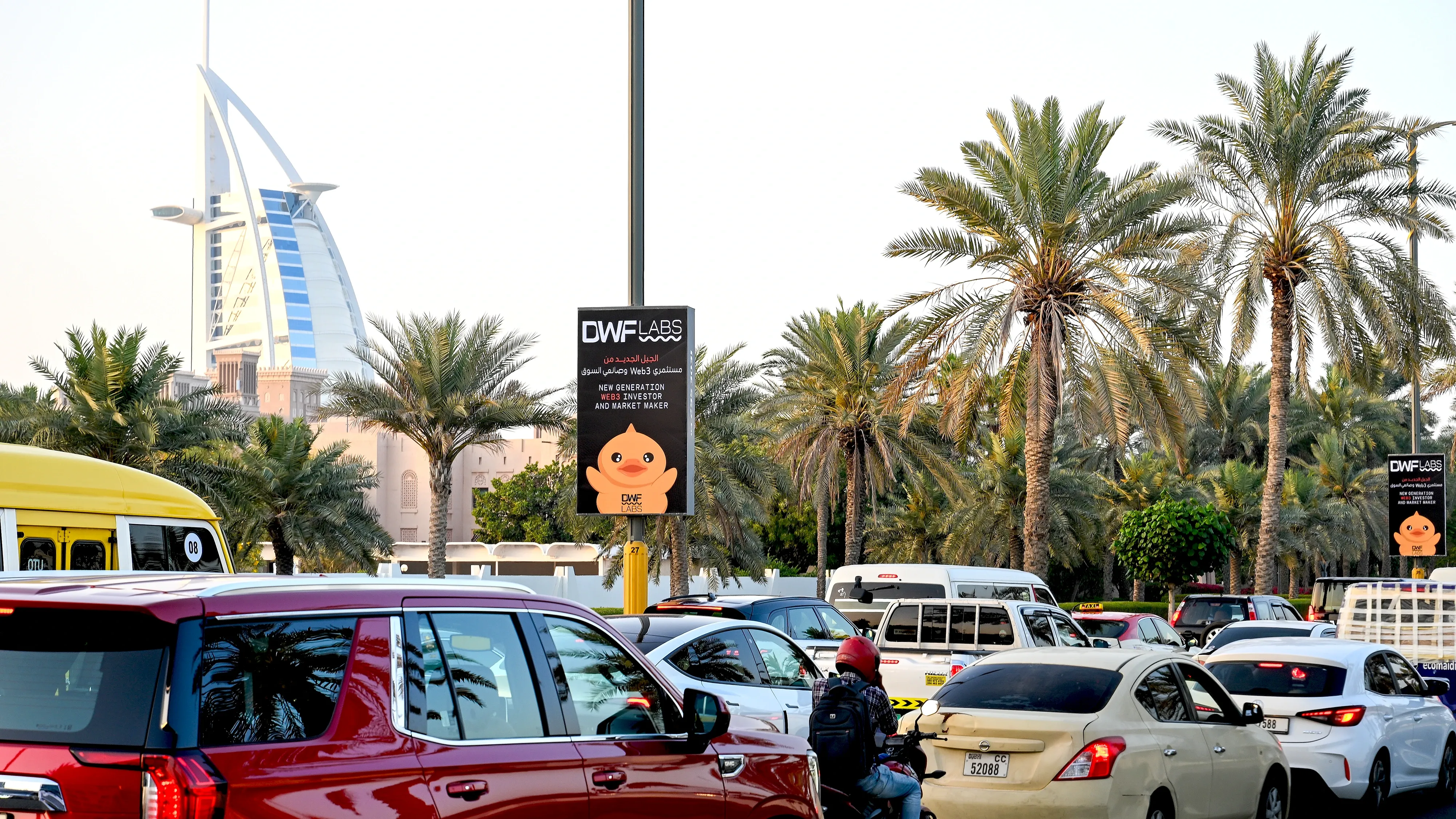 DWF Labs lamppost advertising campaign near Burj Al Arab, Dubai — vertical roadside streetlight banner promoting Web3 investor and market maker brand in high-traffic urban location with palm trees and vehicles.